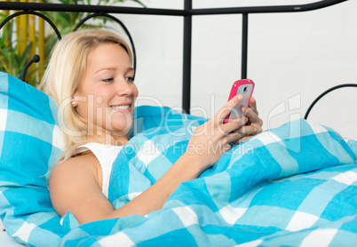 Frau simst im Bett mit Handy