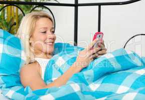 Frau simst im Bett mit Handy