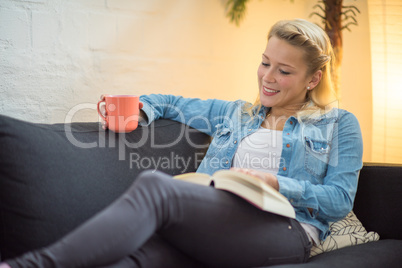 Frau sitzt auf dem Sofa mit Kaffee und Buch