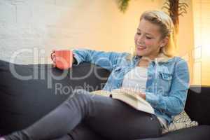 Frau sitzt auf dem Sofa mit Kaffee und Buch