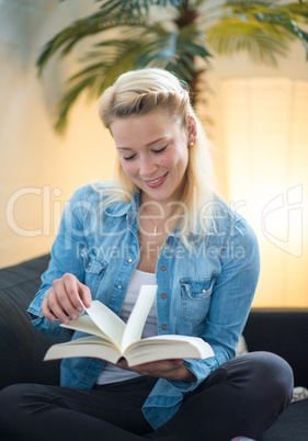 Blonde Frau sitzt auf dem Sofa und liest ein Buch