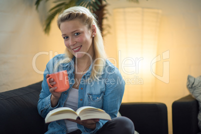 Frau sitzt auf dem Sofa mit Kaffee und Buch