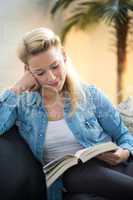 Blonde Frau sitzt auf dem Sofa und liest ein Buch