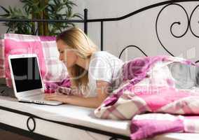 Blonde Frau liegt mit Laptop im Bett