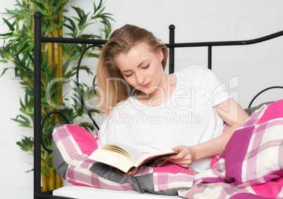 Blonde Frau liest im Bett ein Buch