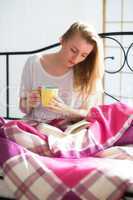 Frau mit Kaffee und Buch im Bett