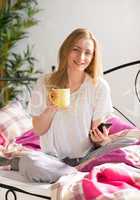 Frau mit Kaffee im Bett simst mit Handy