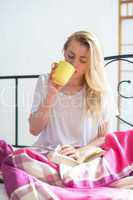 Eine Frau sitzt mit Kaffee und Buch im Bett