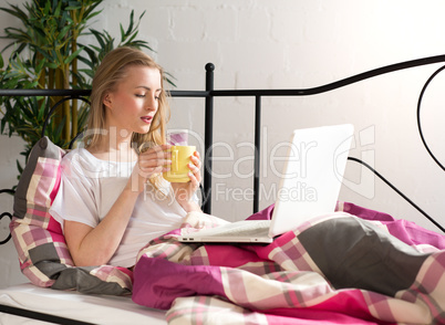 Frau mit Laptop im Bett trinkt Kaffee