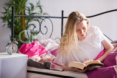 Blonde Frau liest im Bett ein Buch