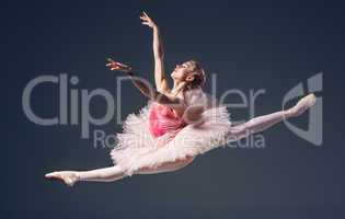 Beautiful female ballet dancer on a grey background. Ballerina is wearing  pink tutu and pointe shoes.