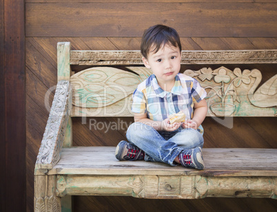 Cute Mixed Race Boy Sitting on Bench Eating Sandwich