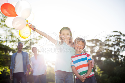 Happy siblings holding balloons at the park