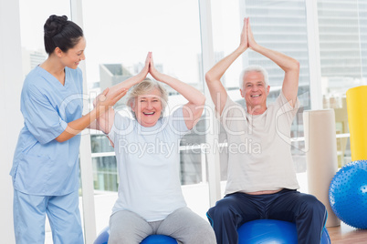 Senior couple on exercis ball being assisted by trainer