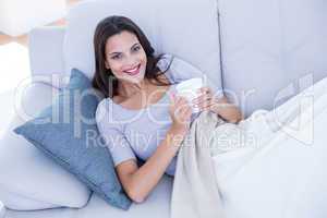 Smiling beautiful brunette relaxing on the couch and holding mug