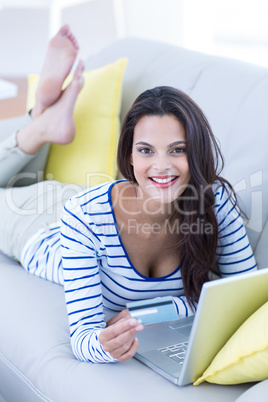 Smiling beautiful brunette doing online shopping on the couch