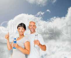 Composite image of fit couple with water bottles gesturing thumb