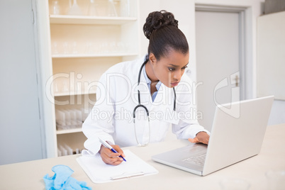 Scientist taking notes while using laptop
