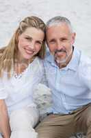 Happy couple sitting on the sand and looking at the camera