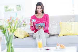 Smiling beautiful brunette doing online shopping on the couch