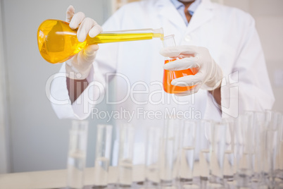 Concentrated scientist pouring orange fluid