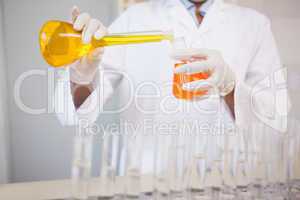 Concentrated scientist pouring orange fluid