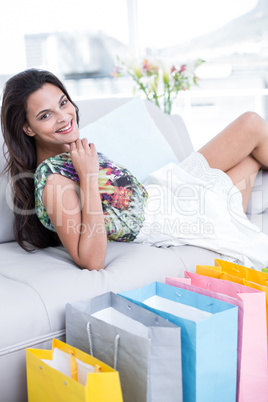 Smiling beautiful brunette lying on the couch with shopping bags