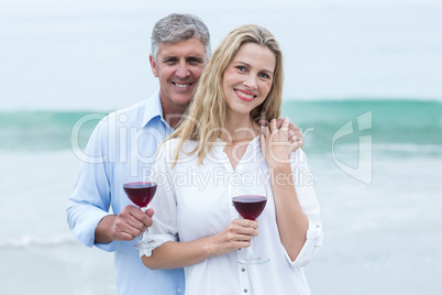 Happy couple smiling at camera and holding a glass of red wine