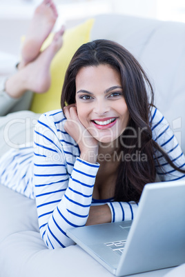 Smiling beautiful brunette relaxing on the couch and using her l