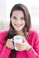 Smiling beautiful brunette relaxing on the couch and holding mug