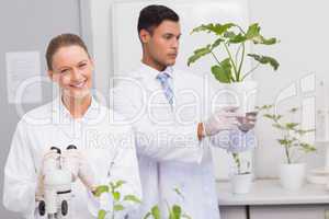 Scientist smiling at camera while colleague looking at plant