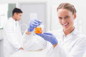 Smiling scientist looking at camera and holding beaker with oran