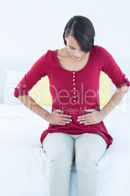 Pretty brunette sitting on bed with stomach pain