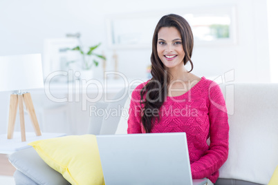 Smiling beautiful brunette using her laptop on the couch