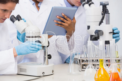 Scientists working with microscope and tablet