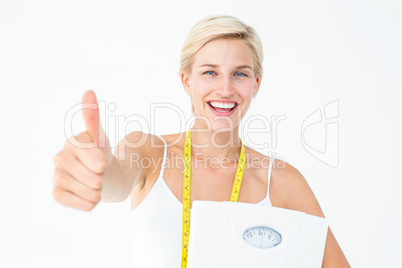 Happy woman holding scales with thumbs up
