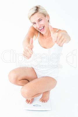 Happy blonde woman crouching on a scales with thumbs up