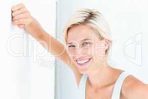 Happy woman smiling at camera with hand on wall
