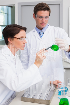 Scientists examining attentively beaker with green fluid