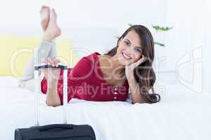 Beautiful woman with a suitcase lying on her bed