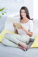 Smiling beautiful brunette relaxing and reading a book on the co