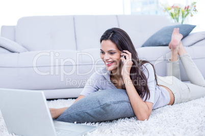 Smiling beautiful brunette lying on the floor and speaking on th