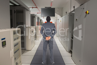 Composite image of young businessman standing with hands behind