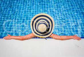 Woman in straw hat relaxing swimming pool