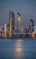 Skyline von Abu Dhabi im Abendlicht mit Wasser im Vordergrund