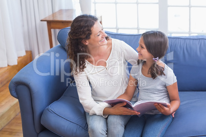 Happy mother and daughter sitting on the couch and reading book