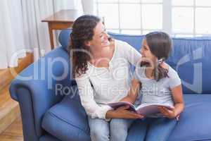 Happy mother and daughter sitting on the couch and reading book