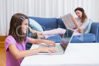 Mother reading news with daughter using laptop