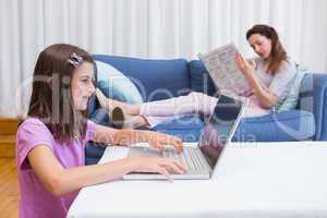 Mother reading news with daughter using laptop