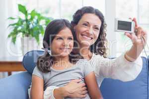 Happy mother and daughter sitting on the couch and taking selfie